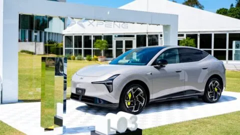 A silver Xpeng L03 SUV displayed on a white platform outside an Xpeng showroom.